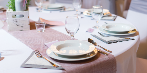A set wedding table with white and maroon linens, silverware, dish sets and glassware.  