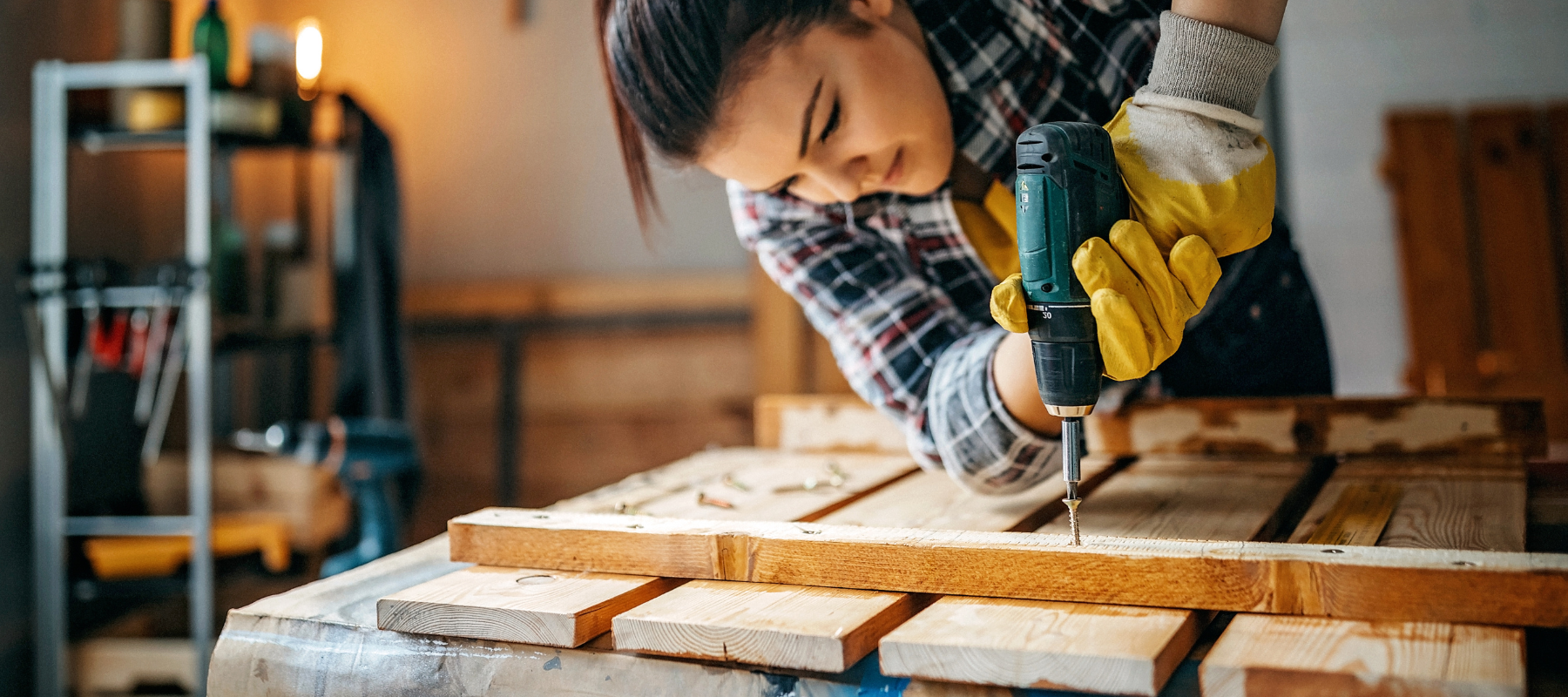 A woman using a power drill on a diy project inside of a garage.