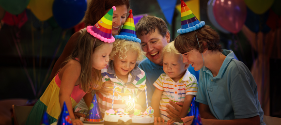 A family gathered around a lit birthday cake, preparing to blow it out.